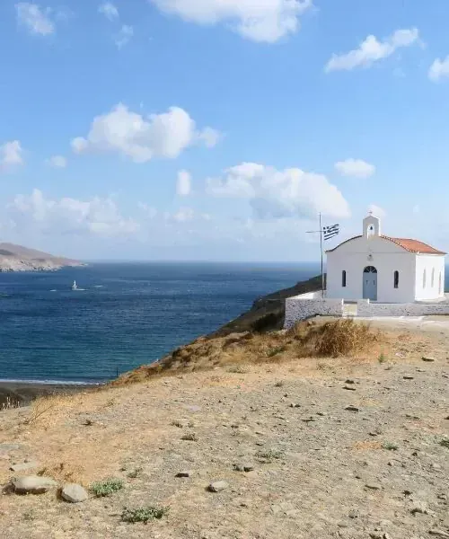 White seaside chapel with Greek flag on coastal hillside - Cyclades - Greece