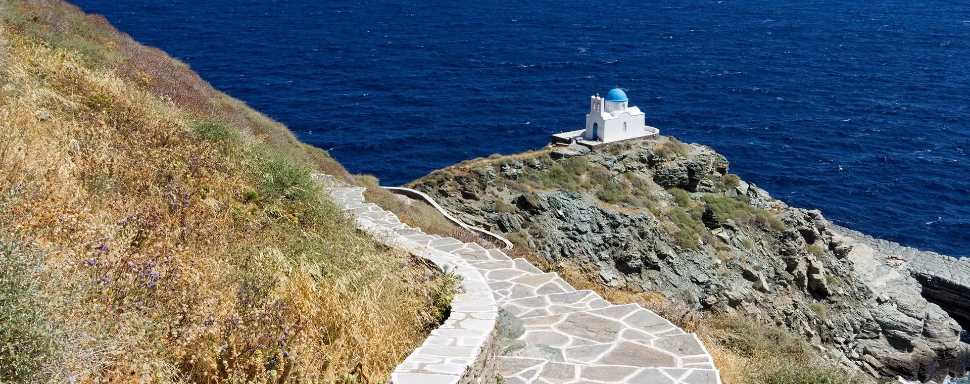 Sentier pavé vers la chapelle Eftamartyres au dôme bleu sur la falaise - Sifnos - Cyclades