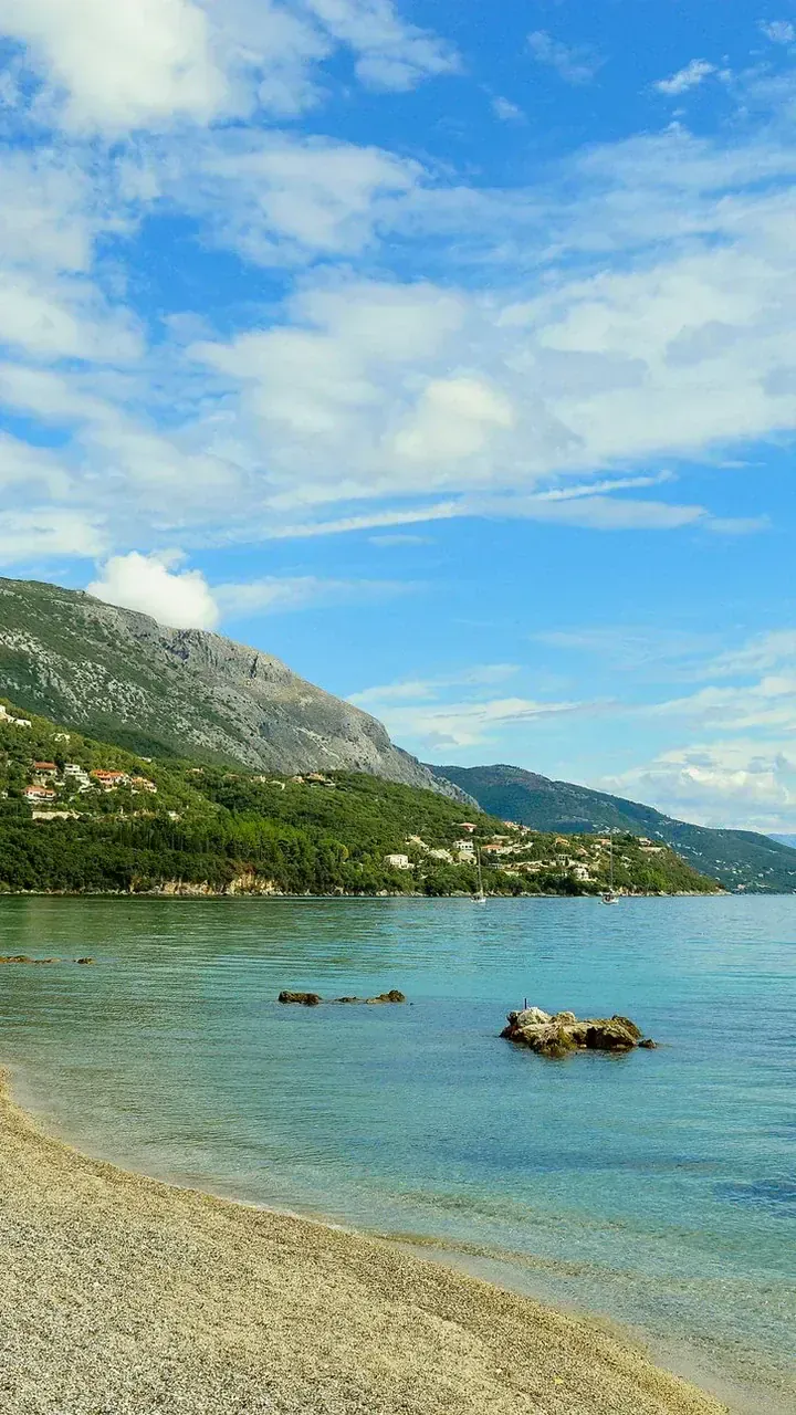 Pebble beach with turquoise water and green mountains - Ipsos - Corfu